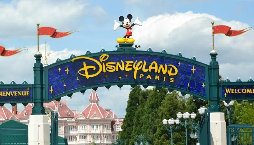 Brama do Disneyland Paris z Myszka Miki na szczycie. W tle różowe budynki i zielone drzewa.
