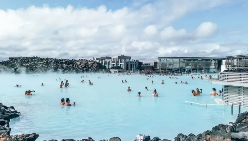 Ludzie kąpią się w turkusowej wodzie geotermalnego **blue lagoon** otoczonej wulkanicznymi skałami.