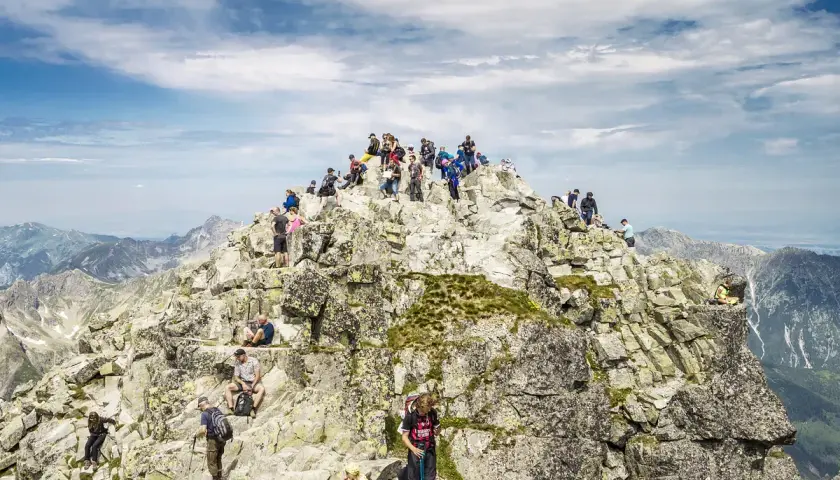 Tłum turystów na skalistym szczycie, najwyższy szczyt w Polsce, podziwia panoramę Tatr.