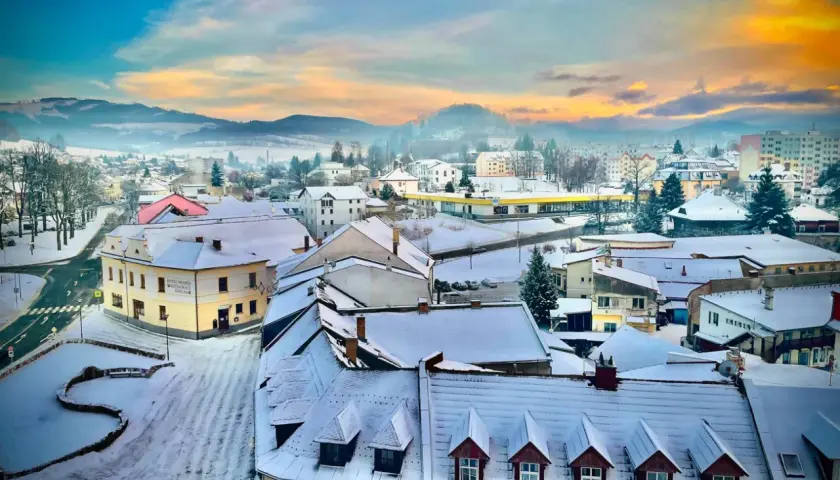 Zimowy krajobraz miasta w Czechach blisko granicy. Śnieg pokrywa dachy i ulice, a w oddali widać mgliste wzgórza.