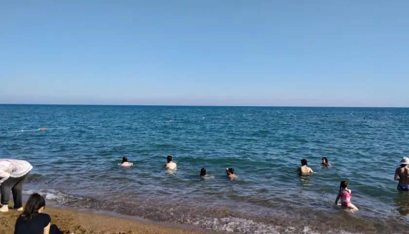 Słoneczny dzień na plaży Lara. Ludzie kąpią się w turkusowym morzu, a na piasku odpoczywają inni plażowicze.