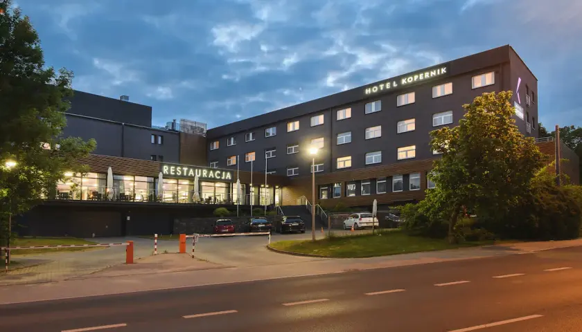 Hotel Kopernik Olsztyn z neonowym napisem "RESTAURACJA" i oświetlonymi oknami. Zapraszamy na nocleg i pyszne jedzenie.