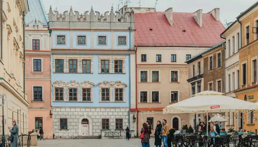 Kolorowe kamienice na rynku, idealne na tani city break. Ludzie spacerują, siedzą w ogródku kawiarnianym.