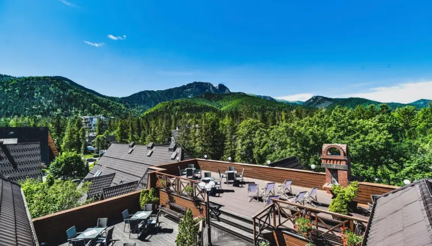 Klimatyczny hotel w górach z tarasem widokowym. Widać drewniane meble, góry i las.