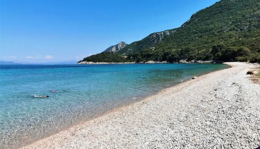 Chorwacja plaże piaszczyste, krystalicznie czysta woda i zielone wzgórza. Dwie osoby pływają w morzu.