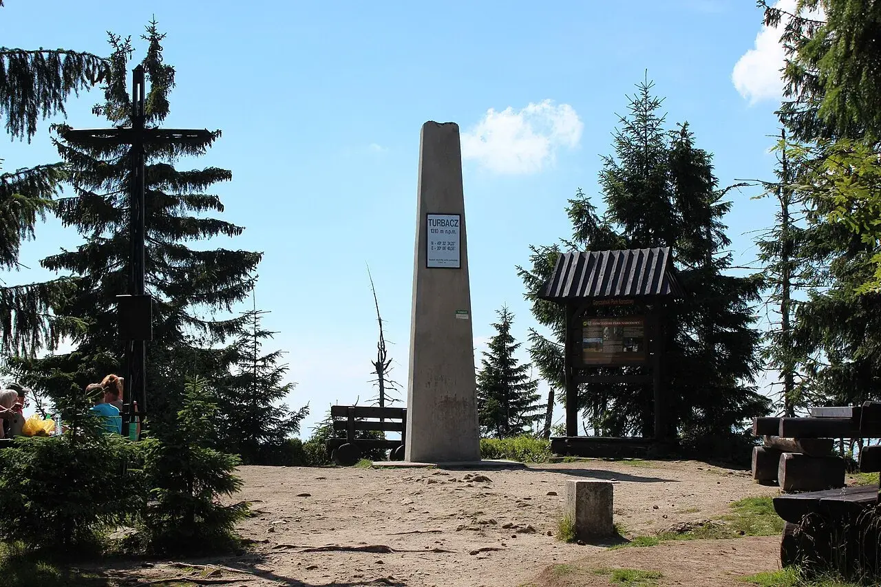 Szczyt Turbacz, 1310 m n.p.m. – ile się idzie? Widok na obelisk, krzyż i tablice informacyjne w otoczeniu górskich lasów.