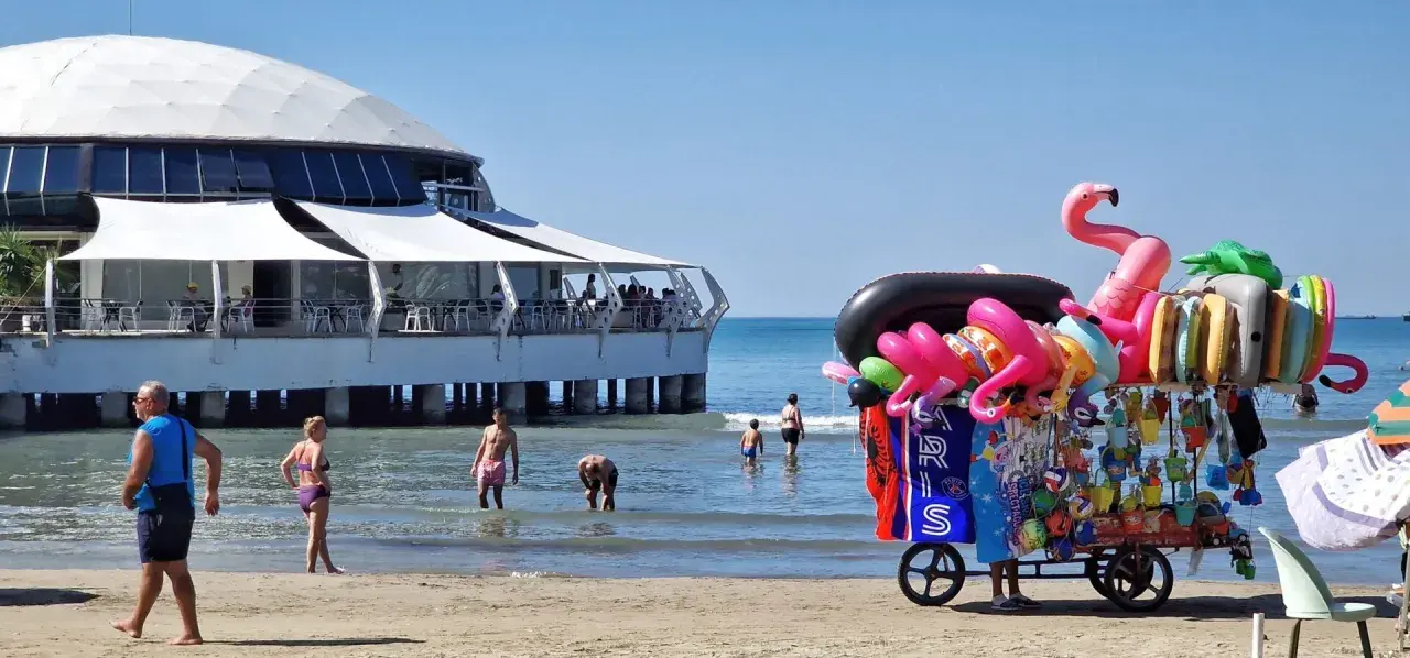 Słoneczna durres plaża z wózkiem pełnym dmuchanych zabawek i restauracją na wodzie.