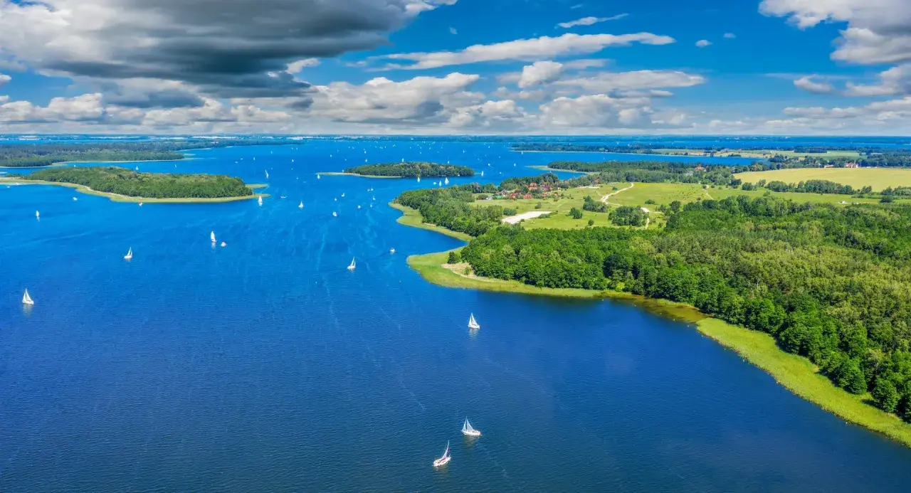 Malownicze jeziora w Polsce, pełne żaglówek pod błękitnym niebem z chmurami. Zielone wyspy i lasy otaczają lazurową wodę.