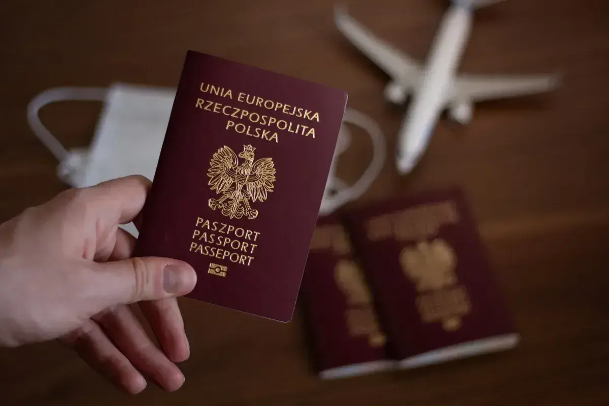 Dłoń trzyma polski paszport. Obok leżą kolejne paszporty, maseczka i samolot. Czas na podróż, ale ile wyrabia się paszport?