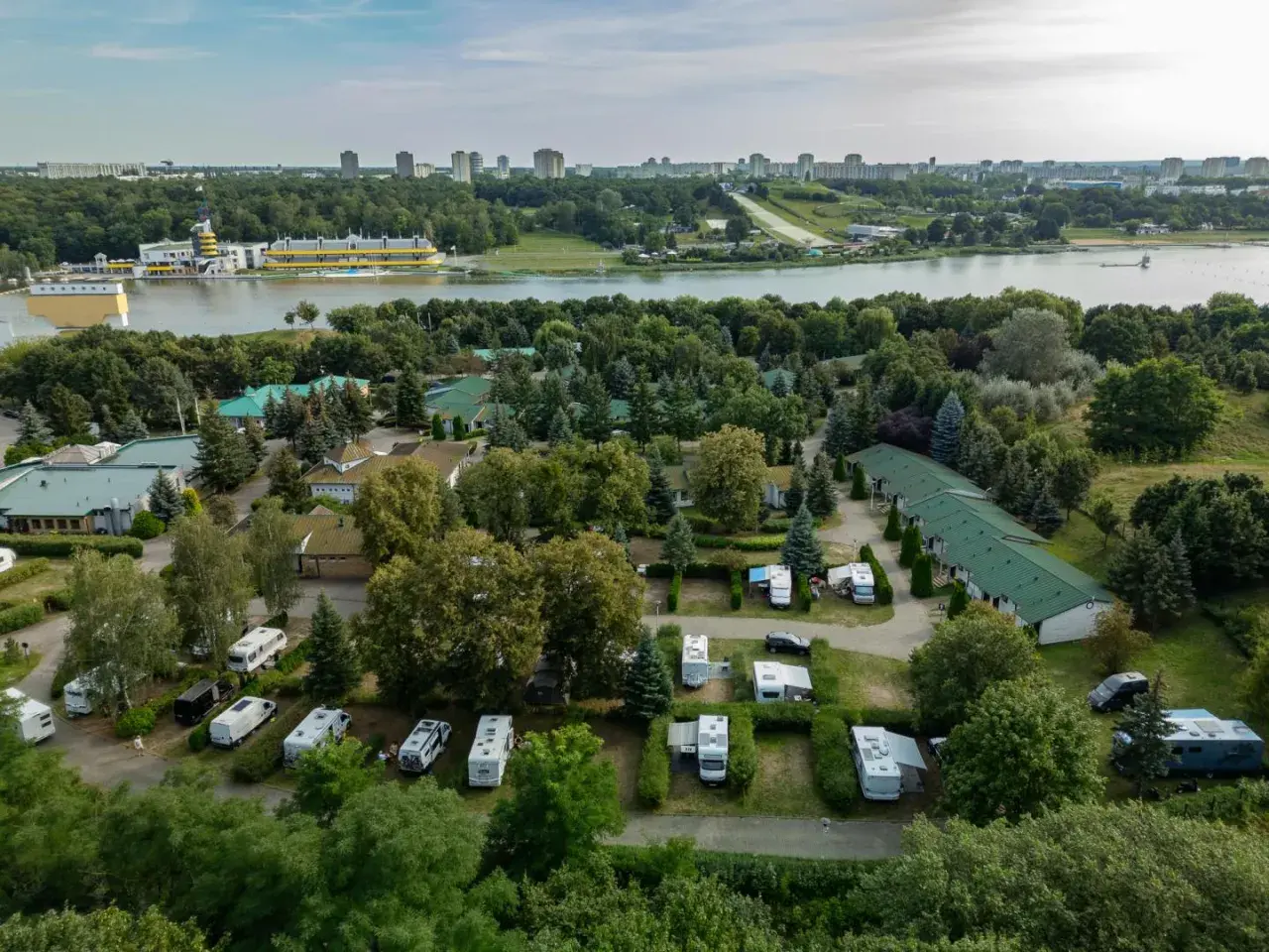 Malta hotel camping: kampery i przyczepy kempingowe wśród zieleni, z widokiem na jezioro i miasto w tle.