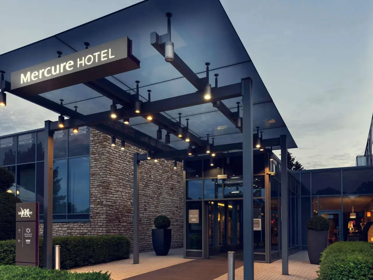 Nowoczesne wejście do hotelu Mercure w Gdańsku, z kamienną fasadą i szklanymi drzwiami.