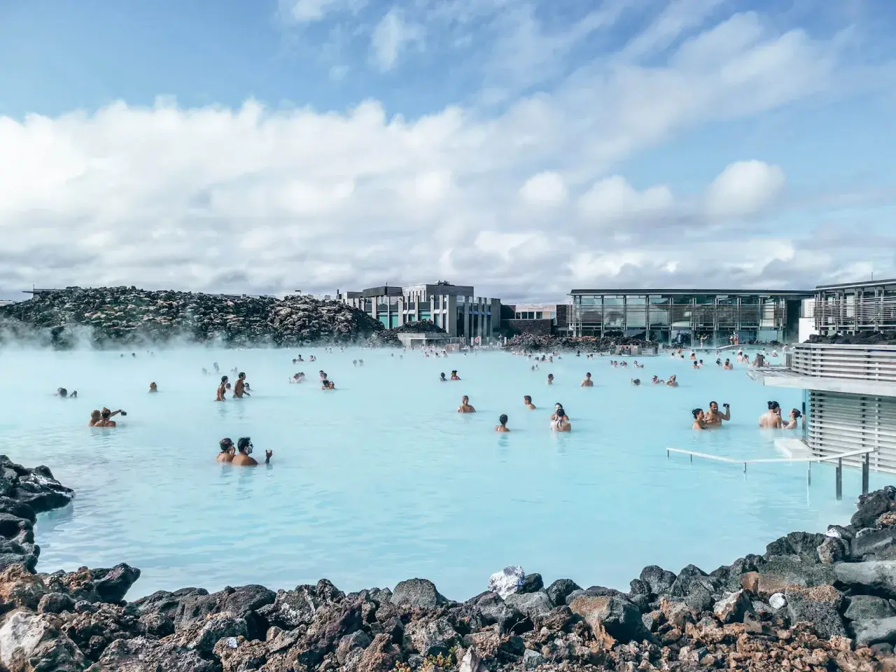 Ludzie kąpią się w turkusowej wodzie geotermalnego **blue lagoon** otoczonej wulkanicznymi skałami.