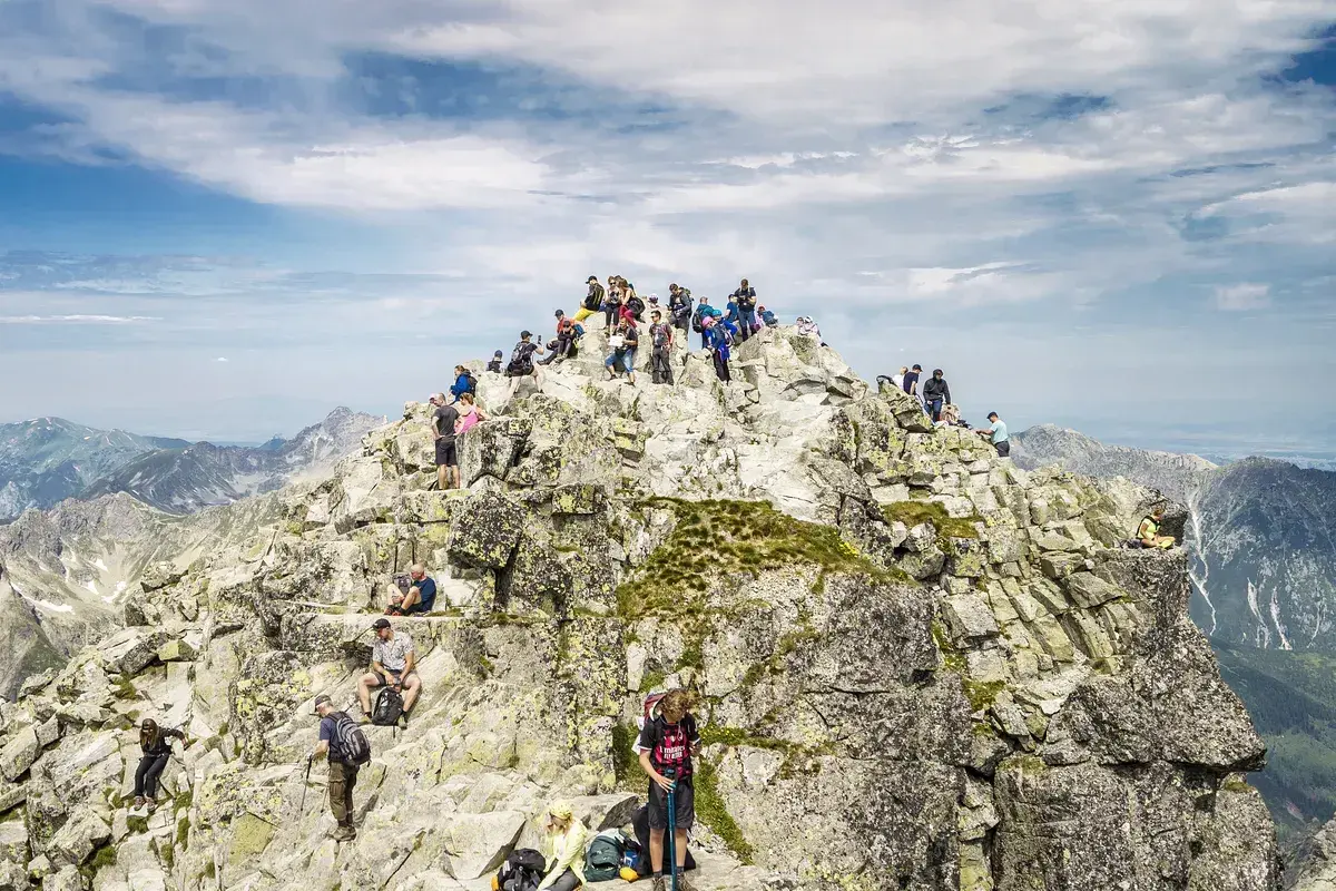 Tłum turystów na skalistym szczycie, najwyższy szczyt w Polsce, podziwia panoramę Tatr.