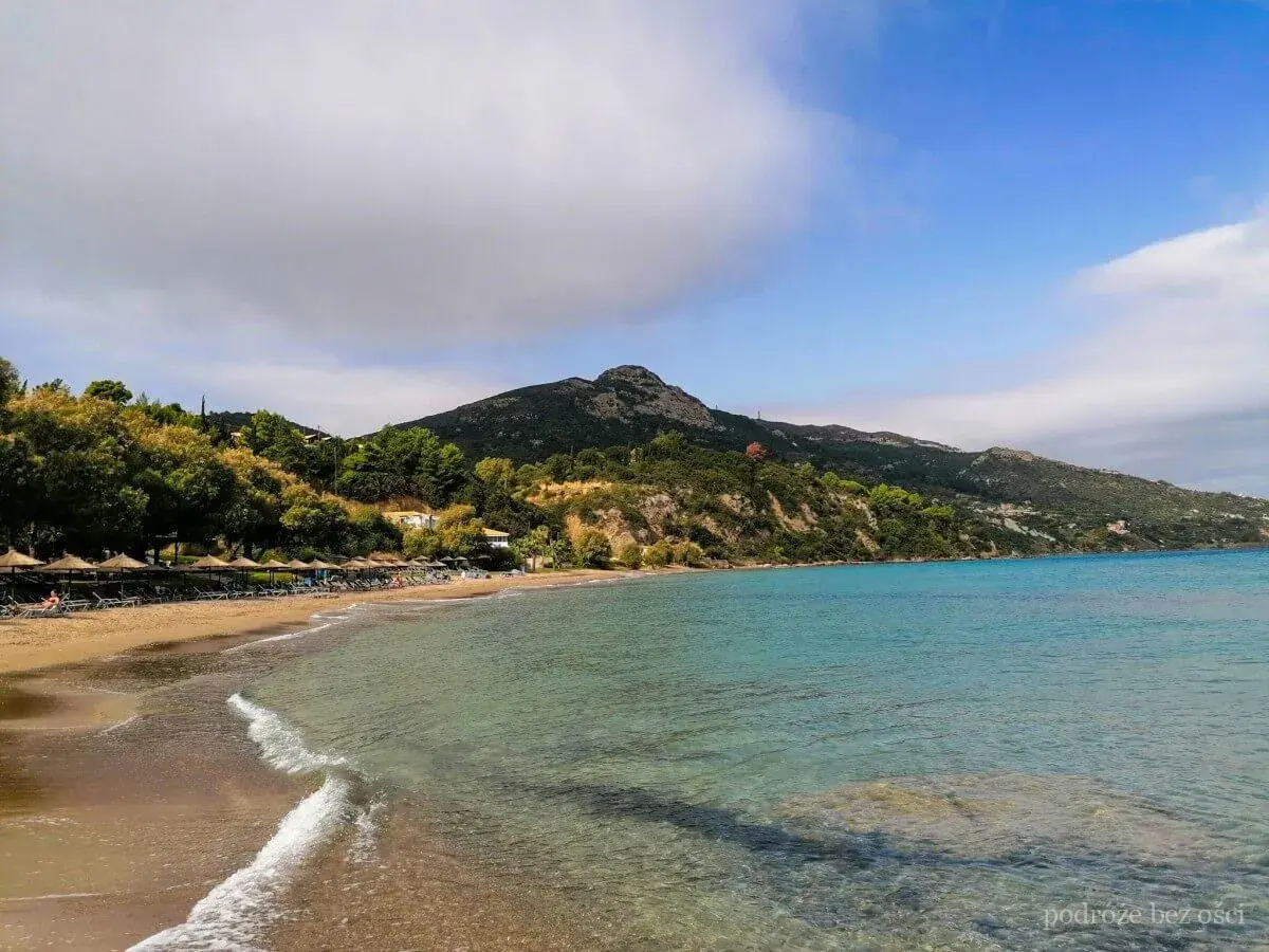 Piękna plaża Tragaki Zakynthos z turkusową wodą, zielonymi wzgórzami i rzędem leżaków pod parasolami.