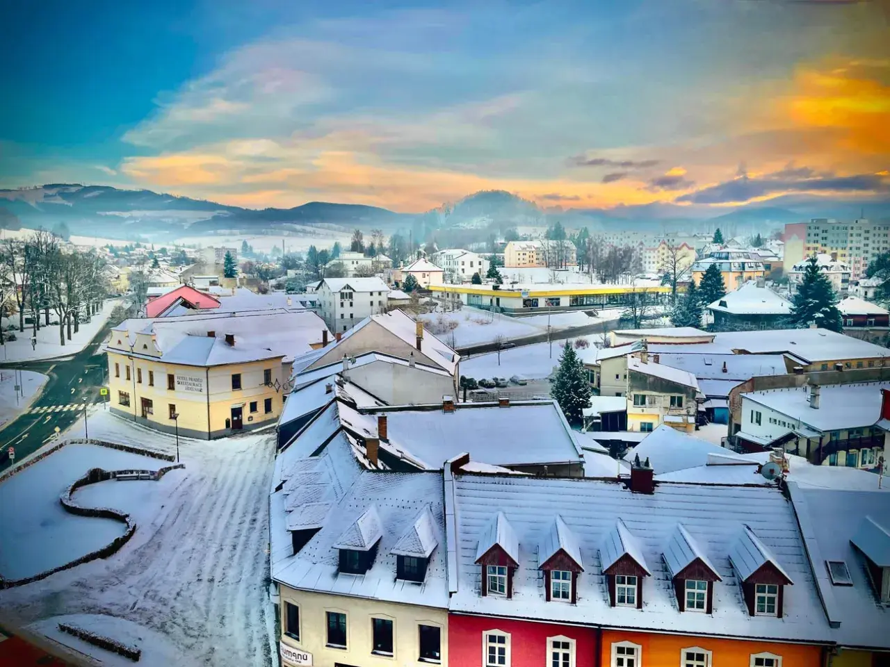 Zimowy krajobraz miasta w Czechach blisko granicy. Śnieg pokrywa dachy i ulice, a w oddali widać mgliste wzgórza.