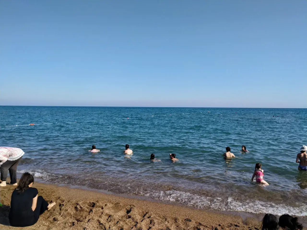 Słoneczny dzień na plaży Lara. Ludzie kąpią się w turkusowym morzu, a na piasku odpoczywają inni plażowicze.