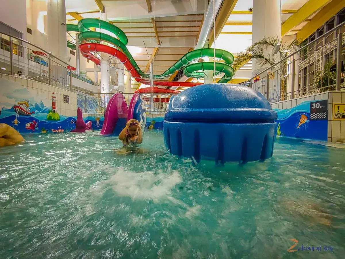 Dziecko bawi się w wodzie w aquaparku hotelu Crocus, w tle kolorowe zjeżdżalnie.