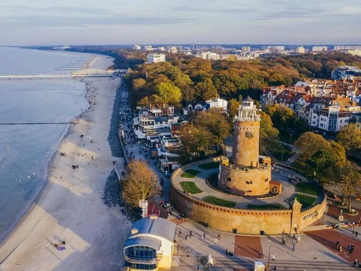 Widok na latarnie morskie w Polsce, z charakterystyczną wieżą w Kołobrzegu, plażą i morzem.