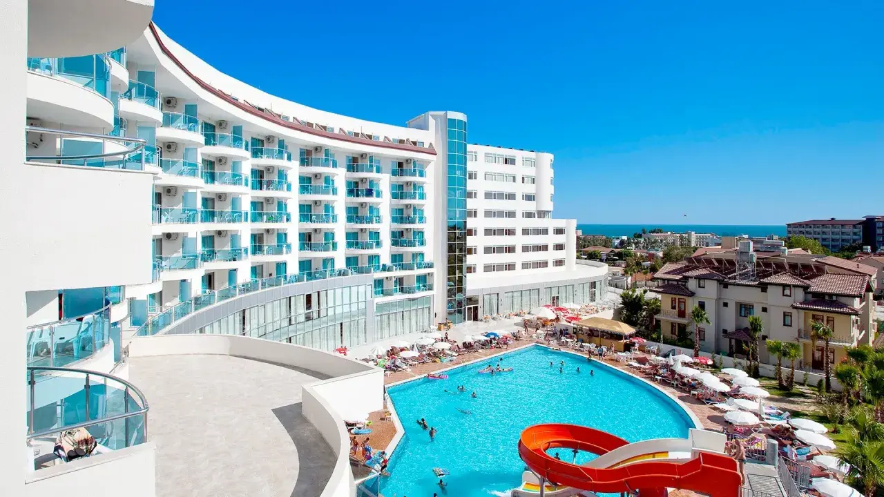 Hotel Narsia Resort: biały, nowoczesny budynek z niebieskimi balkonami i basenem z atrakcjami wodnymi. Słoneczny dzień, wakacyjna atmosfera.