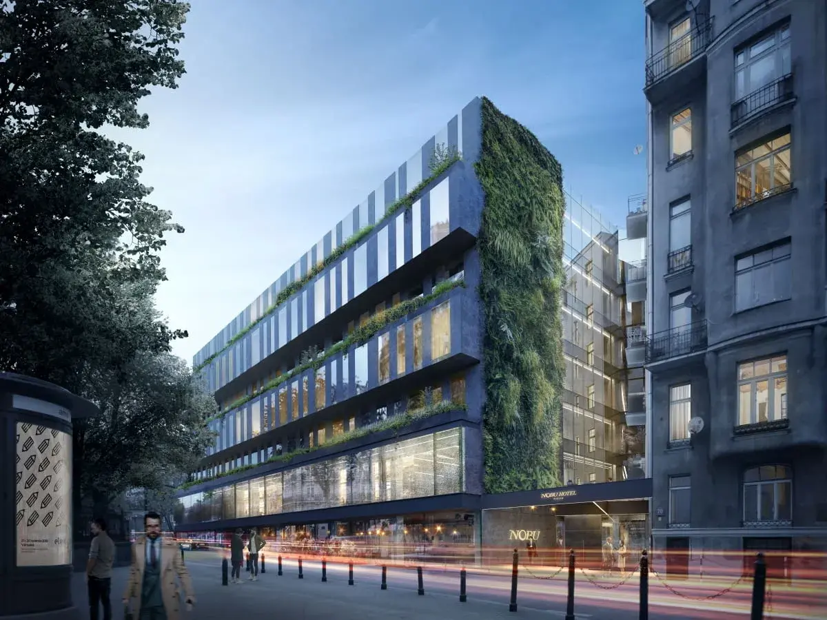 Nowoczesny hotel Nobu Warszawa z zieloną ścianą i przeszklonymi fasadami, otoczony miejską zabudową i drzewami.