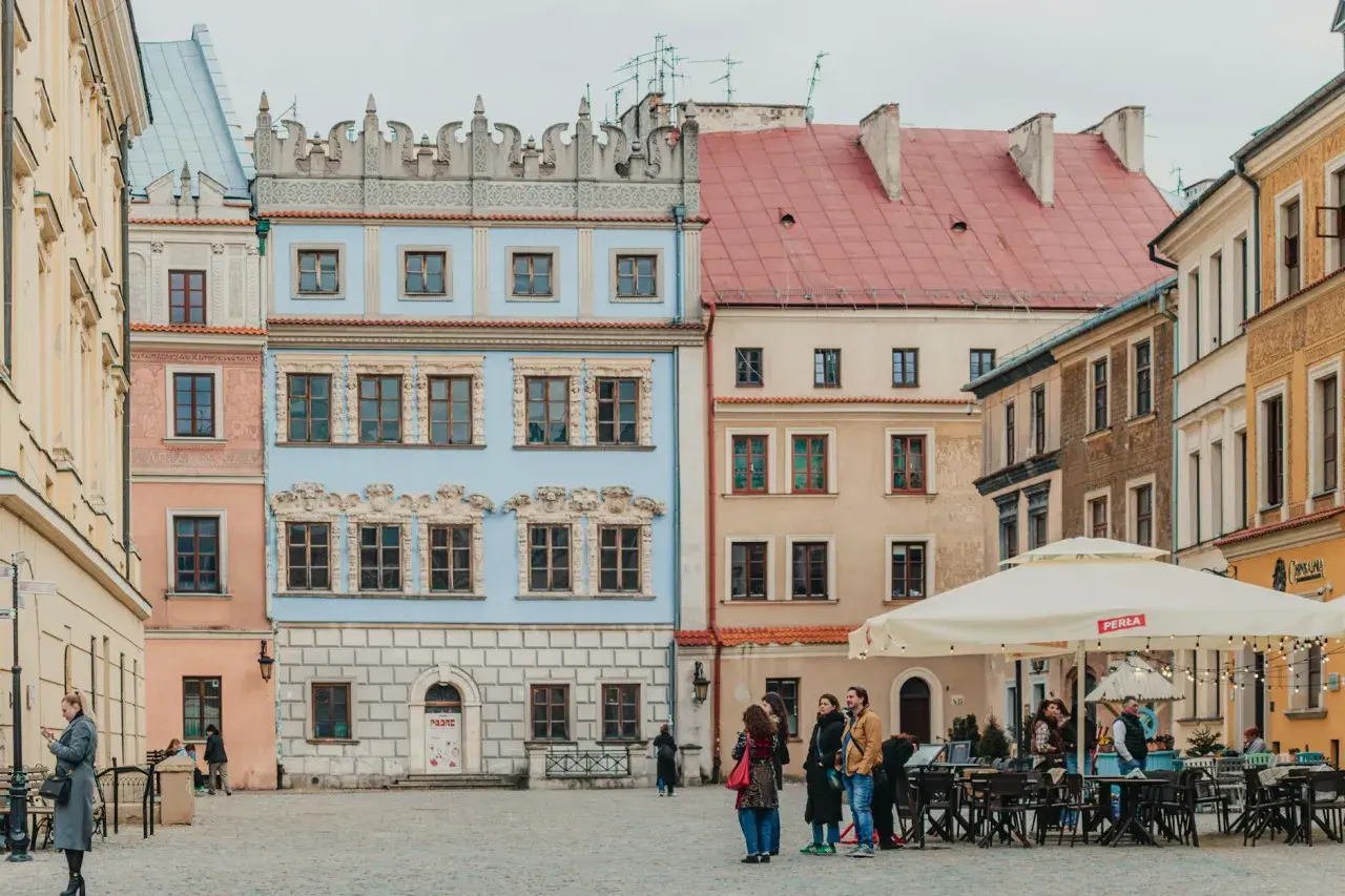 Kolorowe kamienice na rynku, idealne na tani city break. Ludzie spacerują, siedzą w ogródku kawiarnianym.