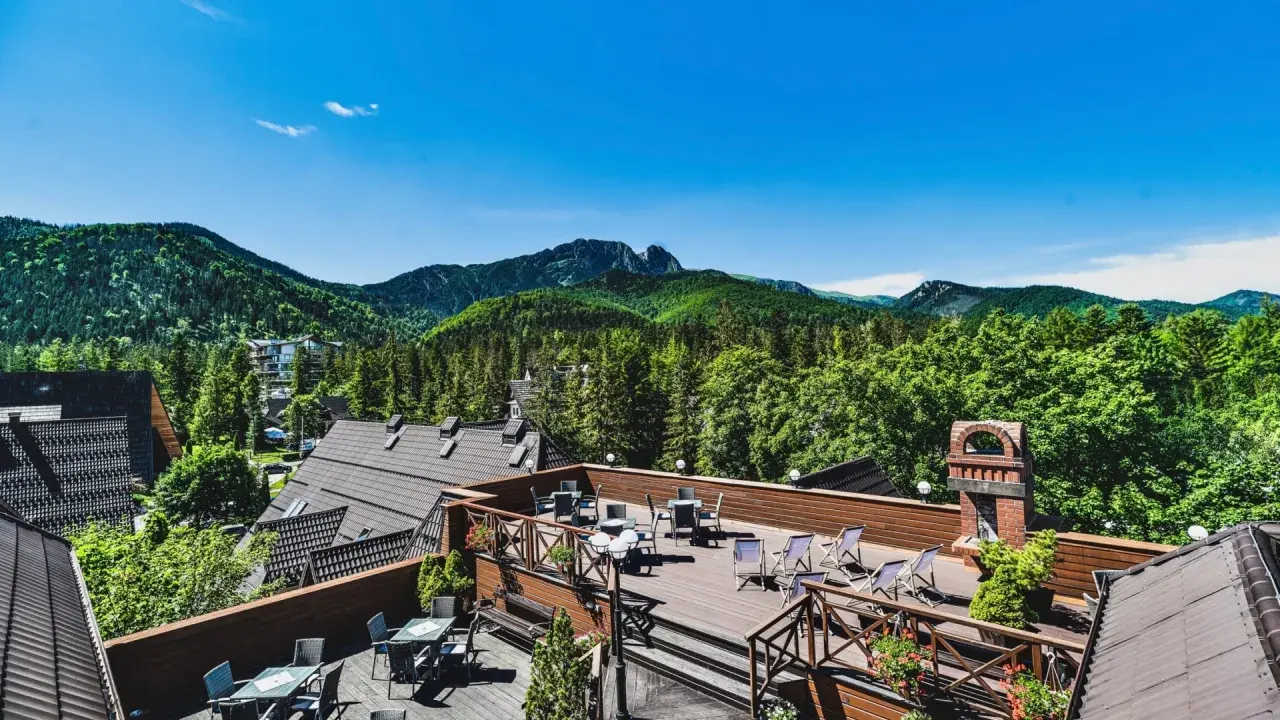 Klimatyczny hotel w górach z tarasem widokowym. Widać drewniane meble, góry i las.