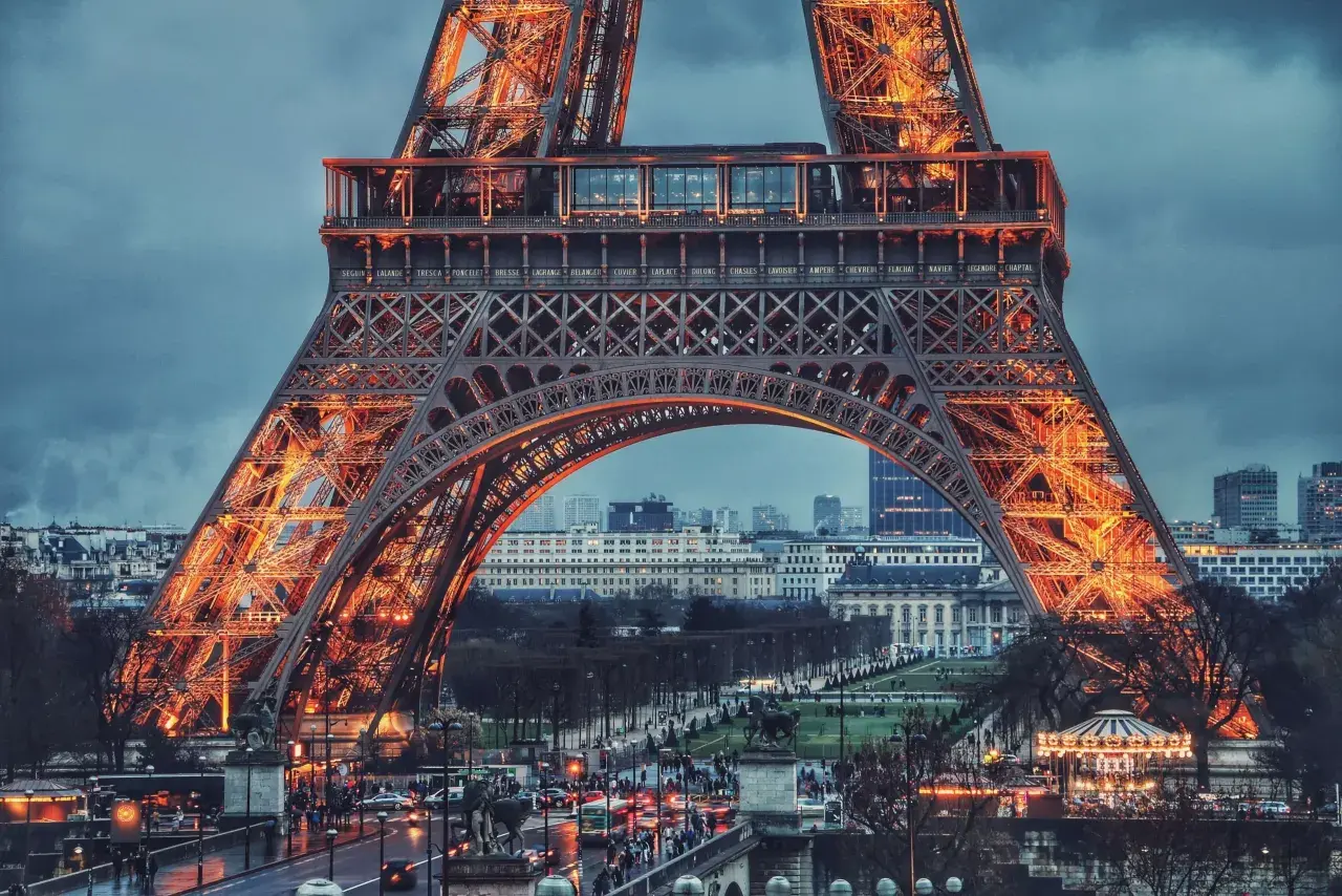 Eiffel rozświetlona pomarańczowym blaskiem, z widokiem na paryskie ulice i budynki.