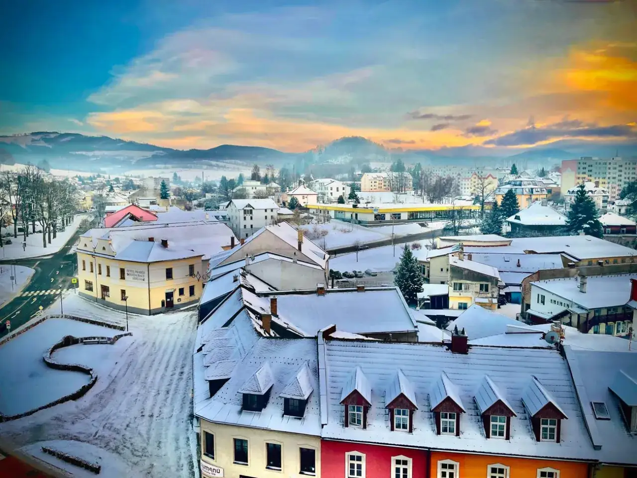 Zimowy krajobraz miasteczka w Czechach blisko granicy. Śnieg pokrywa dachy i ulice, a w oddali widać mgliste wzgórza.