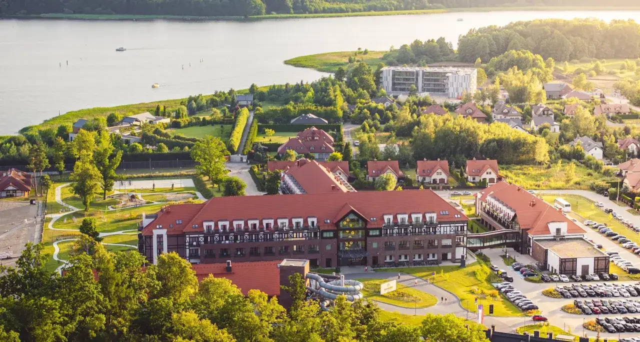 Widok z lotu ptaka na kompleks Radisson z basenami i parkingiem, otoczony zielenią i jeziorem.
