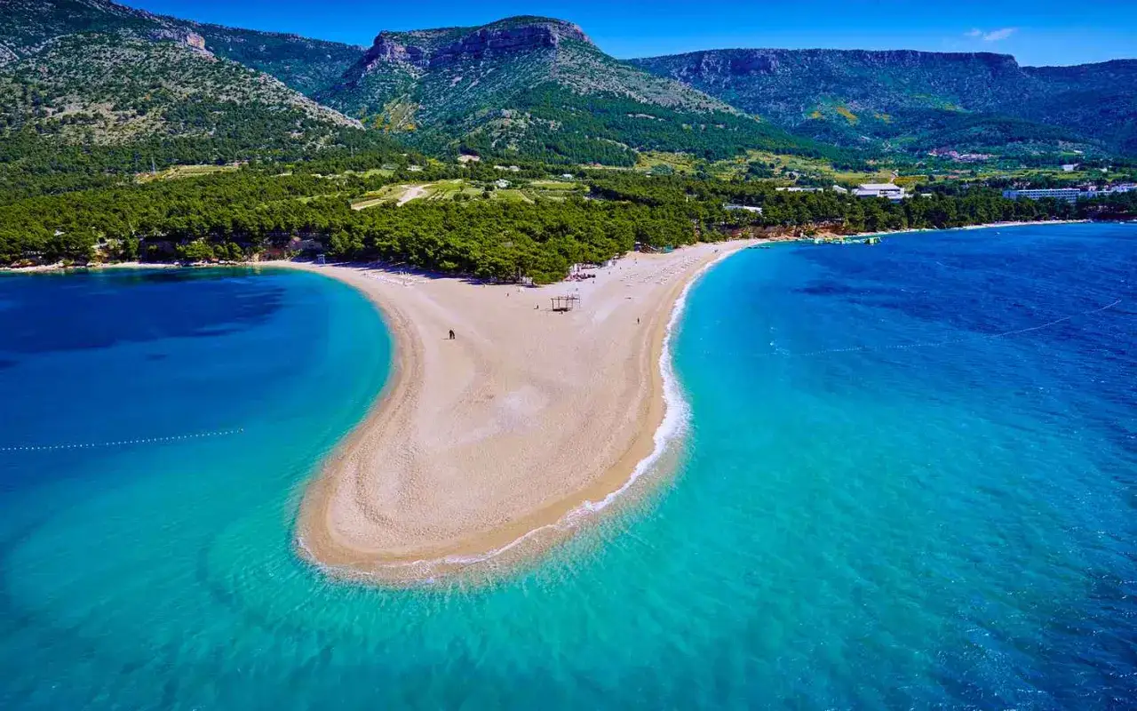 Zlatni Rat, jedna z najpiękniejszych chorwackich plaż piaszczystych, rozpościera się w kształcie rogu obfitości, otoczona turkusowym morzem i zielonymi wzgórzami.