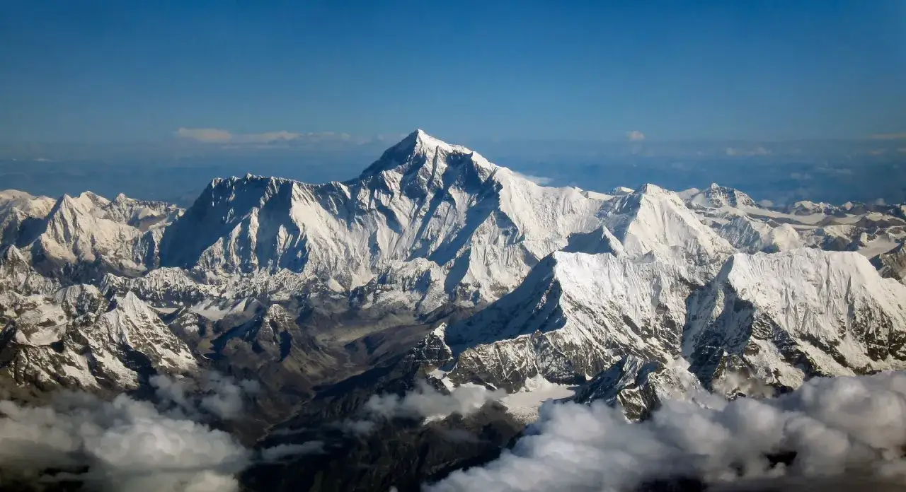 Majestatyczny szczyt Mount Everest, najwyższe góry świata, wznosi się ponad ośnieżonymi pasmami Himalajów, otoczony błękitem nieba i chmurami.