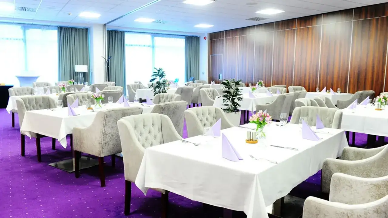 Elegancka sala bankietowa w hotelu Kopernik Olsztyn, z fioletową wykładziną i nakrytymi stołami, gotowa na przyjęcie gości.