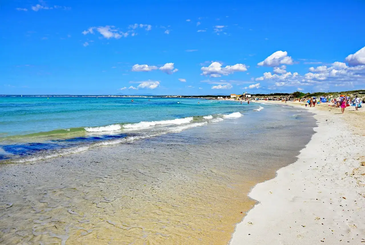 Piękna plaża Es Trenc z turkusową wodą i białym piaskiem, pełna ludzi cieszących się słońcem i morzem.