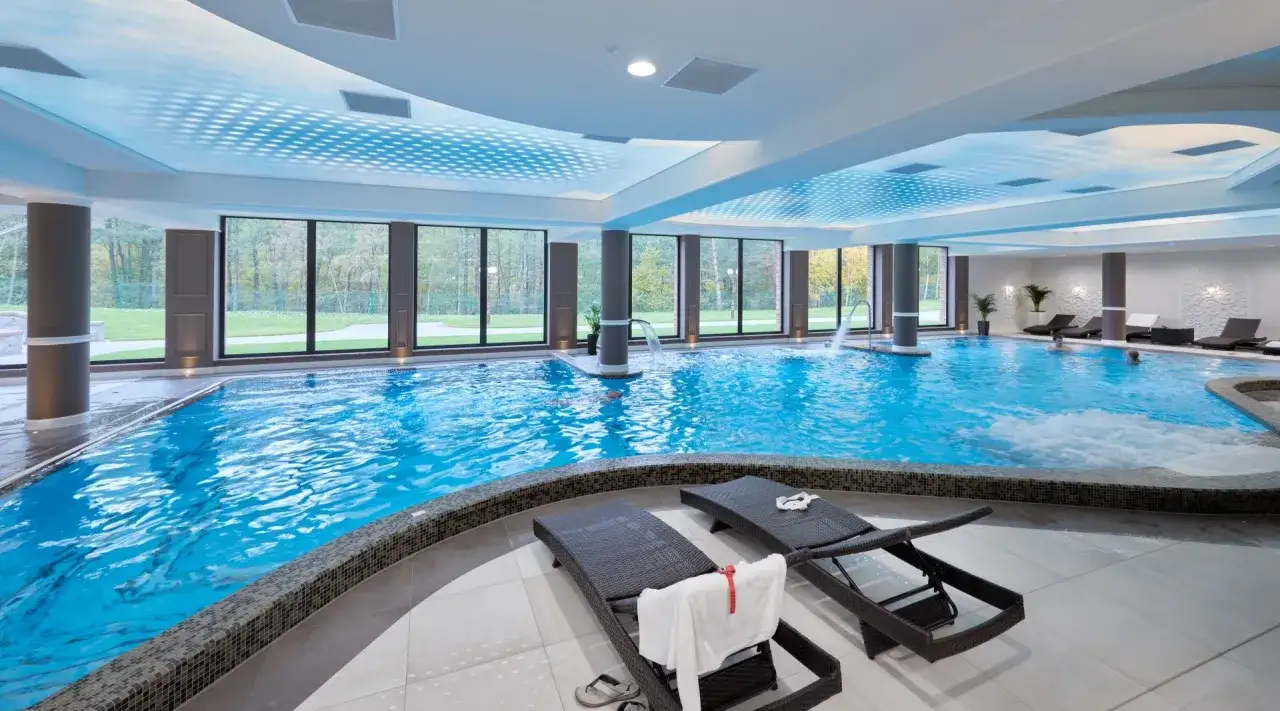 Relaks w basenie Evita Hotel Spa. Dwa leżaki z ręcznikami czekają na gości.