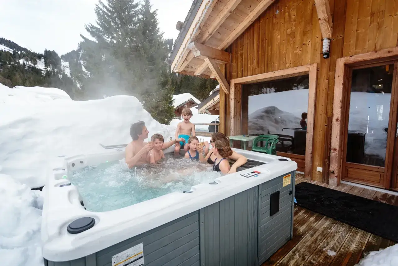 Rodzina w jacuzzi na tle ośnieżonych gór. Idealne miejsce, gdzie pojechać na ferie zimowe za granicę, by połączyć relaks z zimowym szaleństwem.