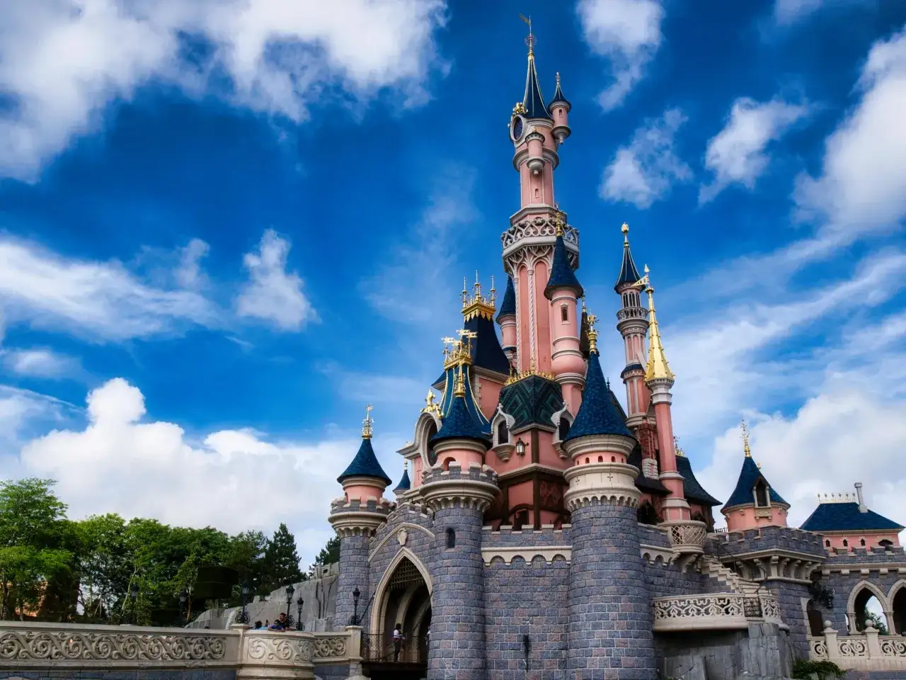 Bajkowy zamek w Disneylandzie, z różowymi wieżami i niebieskimi dachami, pod błękitnym niebem z chmurami.