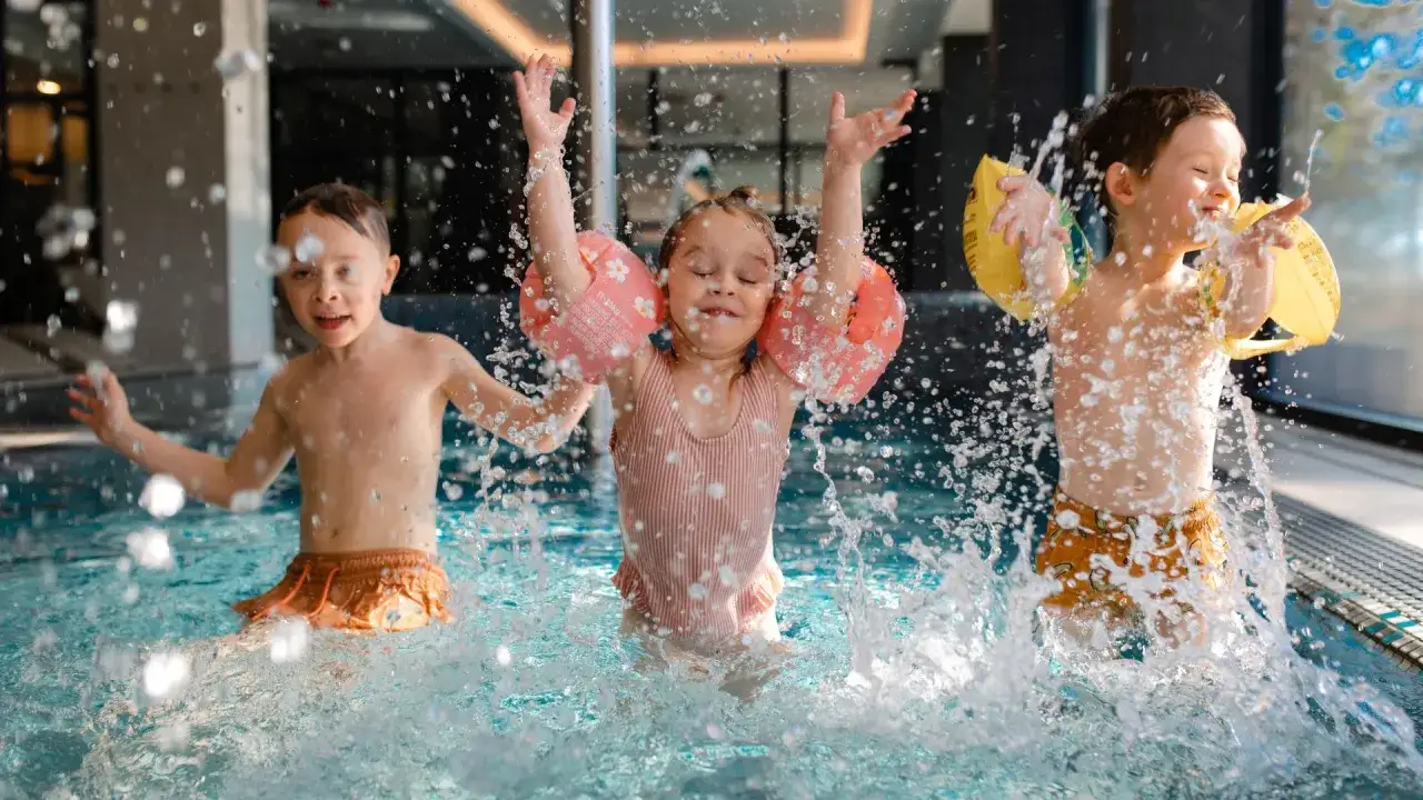 Dzieci szaleją w basenie hotelu z aquaparkiem w górach, chlapiąc wodą i ciesząc się zabawą.