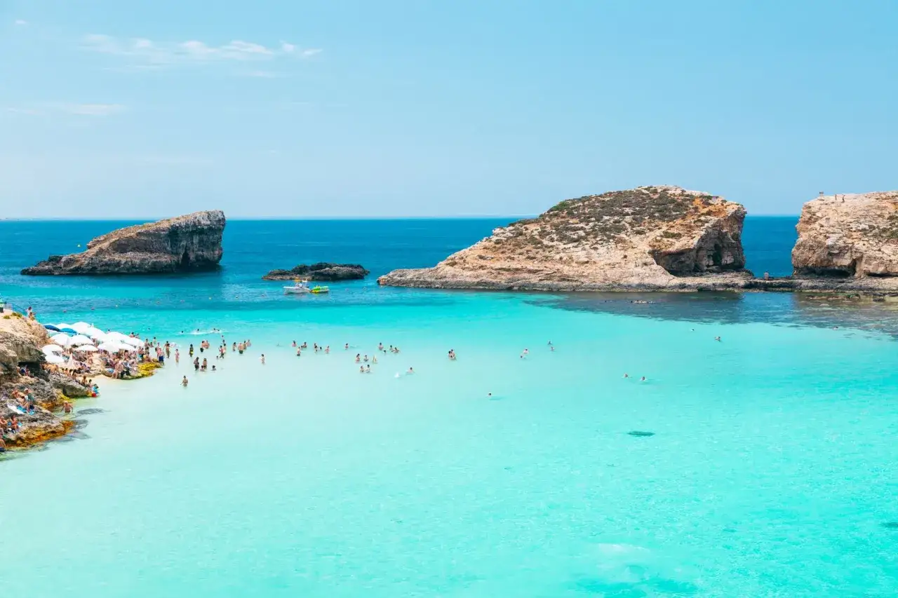 Malta plaże: turkusowa woda, skaliste klify i tłumy plażowiczów cieszących się słońcem.
