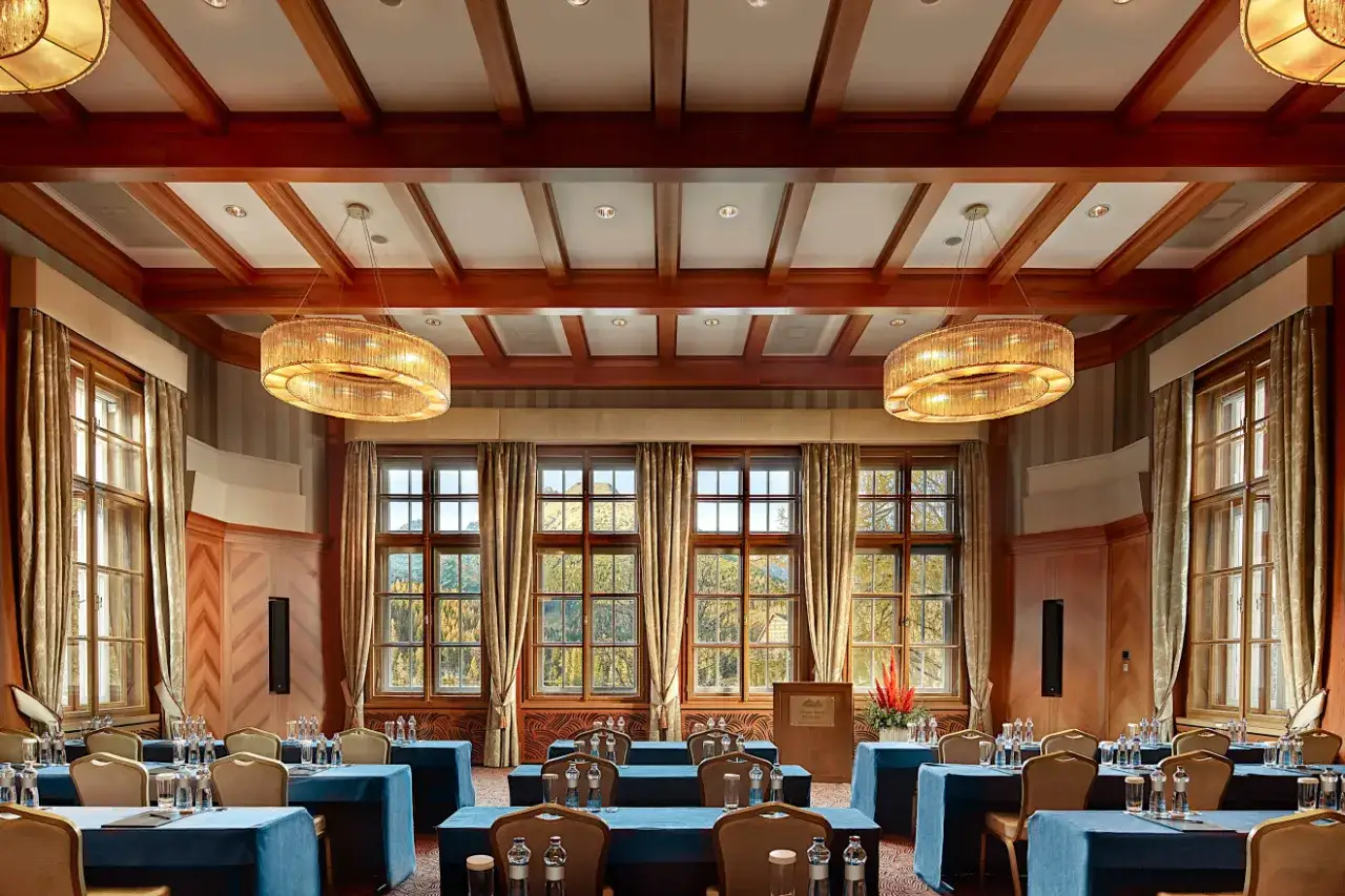 Elegancka sala konferencyjna w Kempinski Hotel, z drewnianymi belkami na suficie, dużymi oknami z widokiem na jesienny krajobraz i stylowymi żyrandolami.