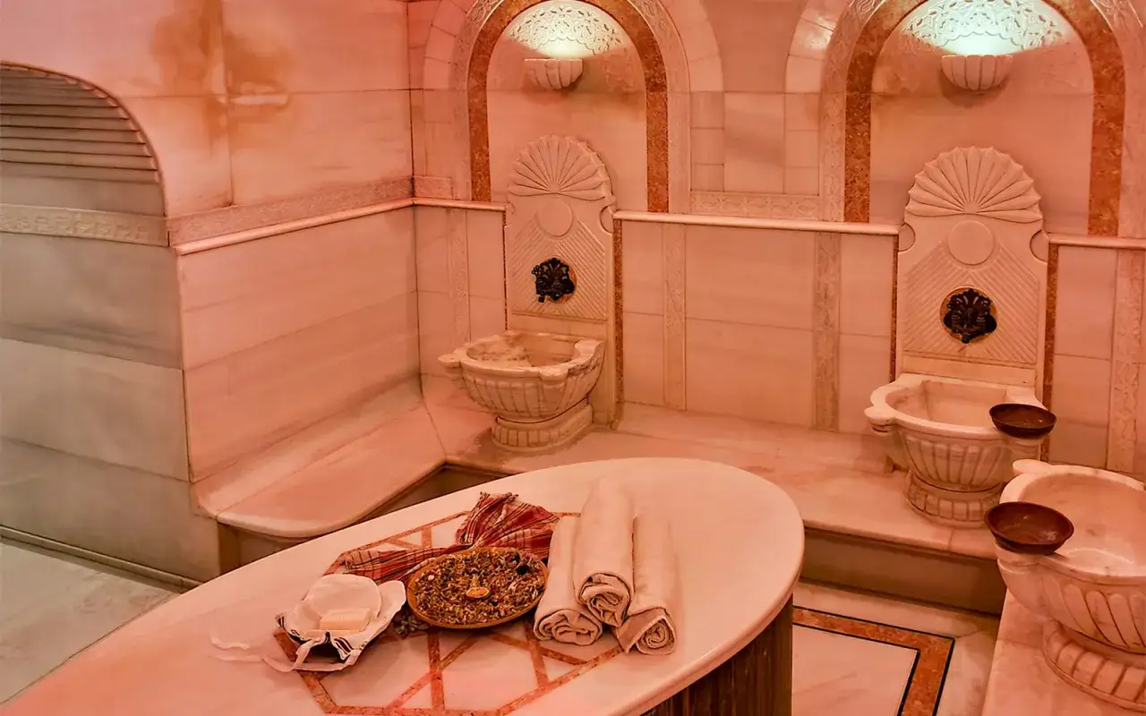 Luksusowy hammam z marmurowymi misami i ozdobnymi kranami. Na stole leżą ręczniki i mydło, gotowe na relaksującą kąpiel.