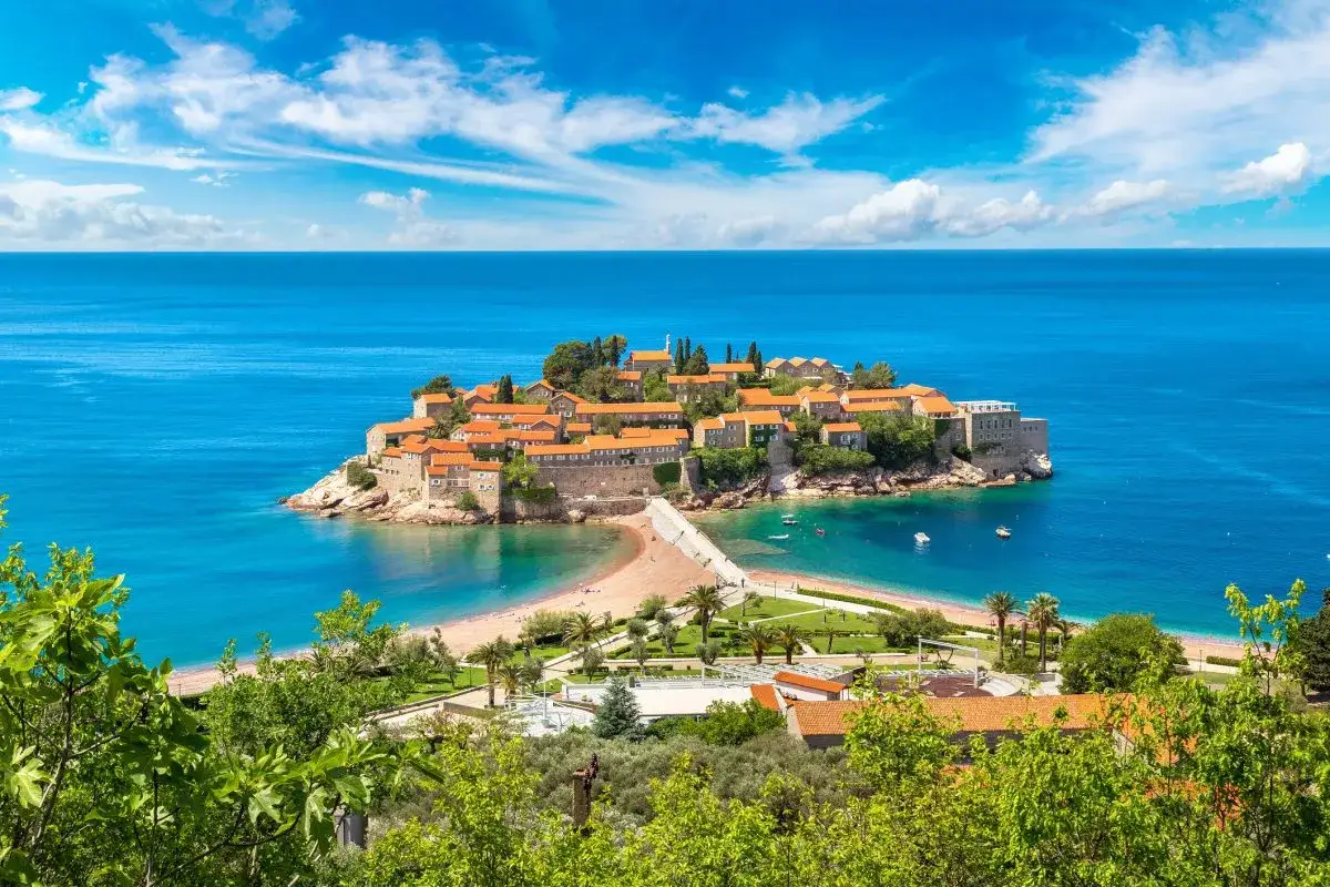 Wyspa Sveti Stefan w Czarnogórze, idealne miejsce na wakacje all inclusive samolotem. Błękitne morze, urokliwe domki i plaża.