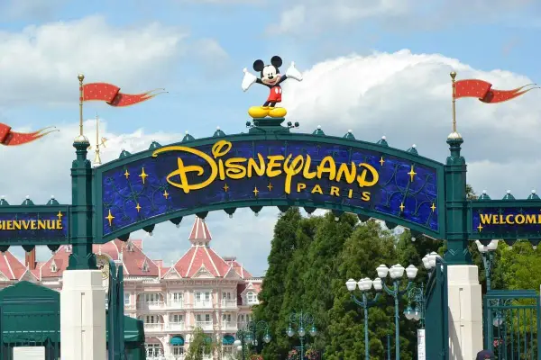 Brama do Disneyland Paris z Myszka Miki na szczycie. W tle różowe budynki i zielone drzewa.